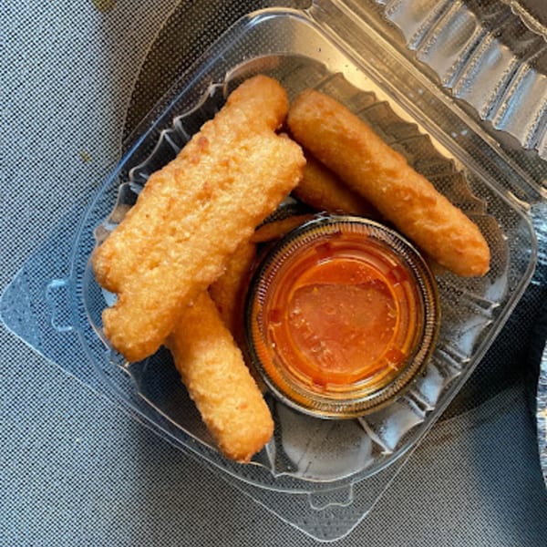 Golden-brown mozzarella sticks and a cup of marinara sauce in a clear plastic container.